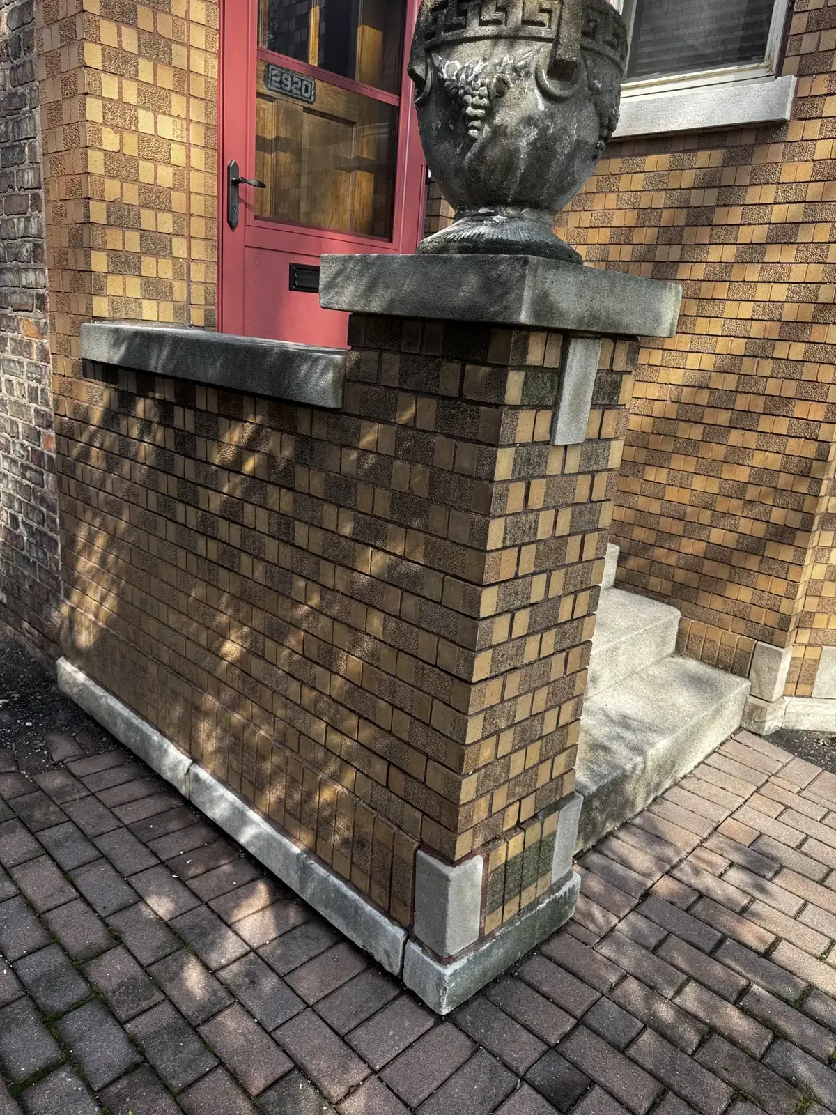 Chicago yellow brick masonry wingwall beside an entrance, with limestone coping caps and a red door