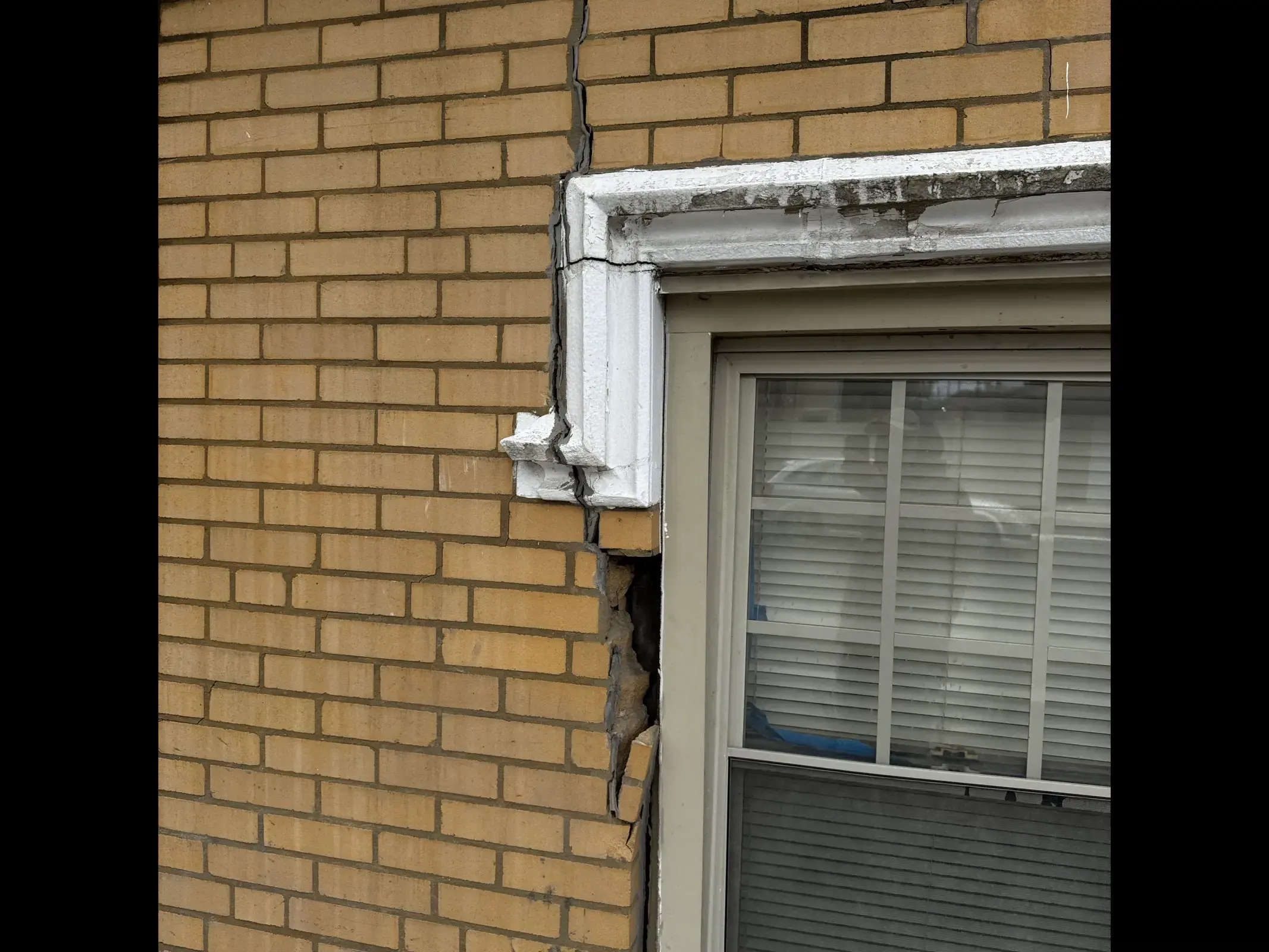 Yellow brick Chicago wall above a window, showing a damaged lintel area and cracked masonry