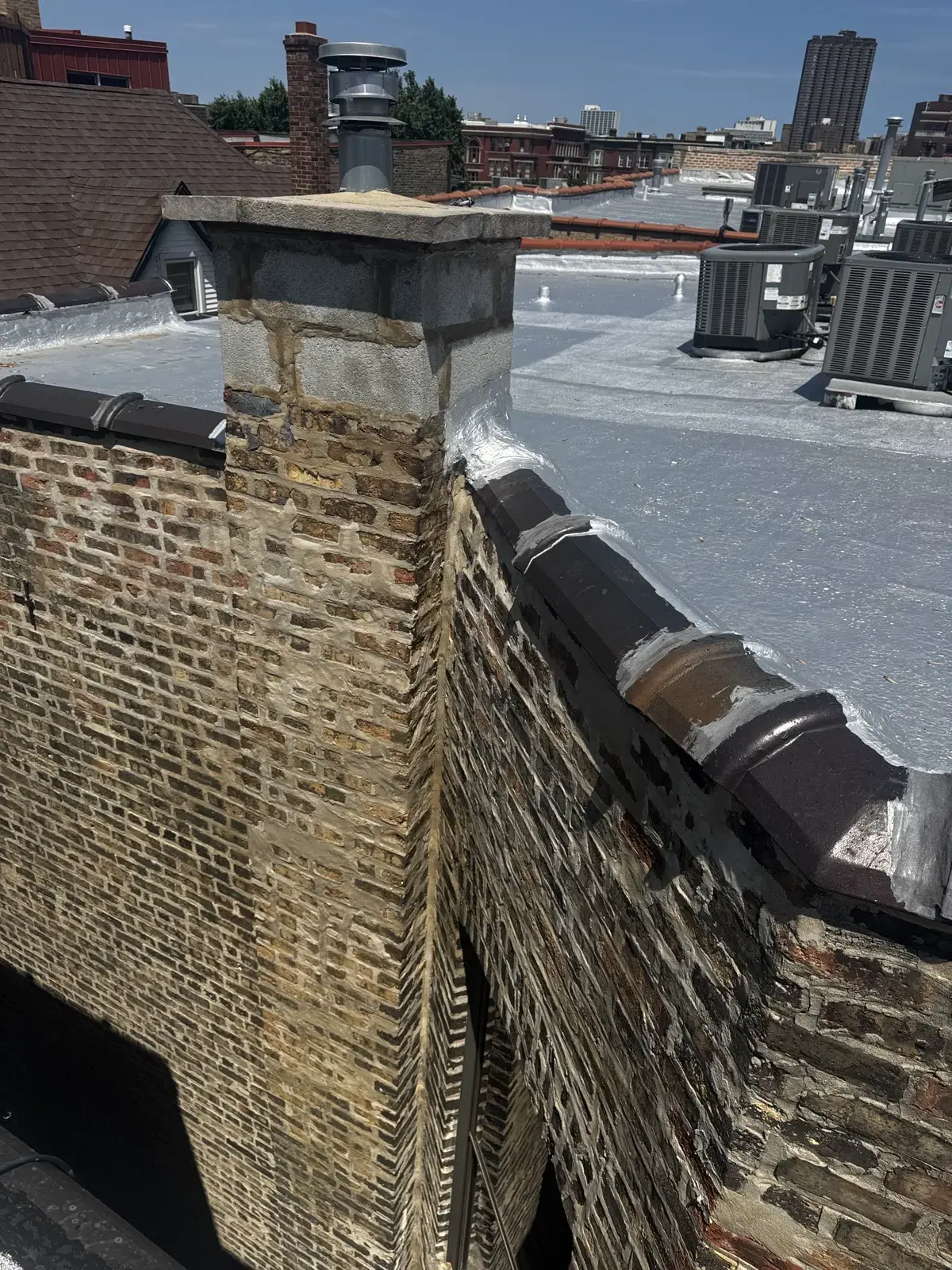 Chicago brick parapet wall above a flat roof, showing the top courses and coping stones