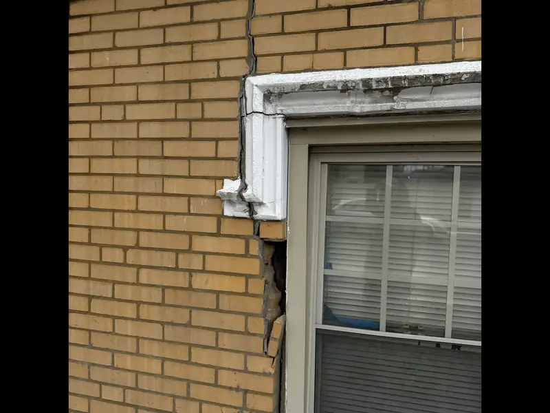 Yellow brick Chicago wall above a window, showing a damaged lintel area and cracked masonry