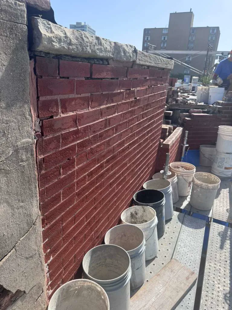 Parapet wall before masonry repair with brickwork, deteriorated mortar, and scaffolding
