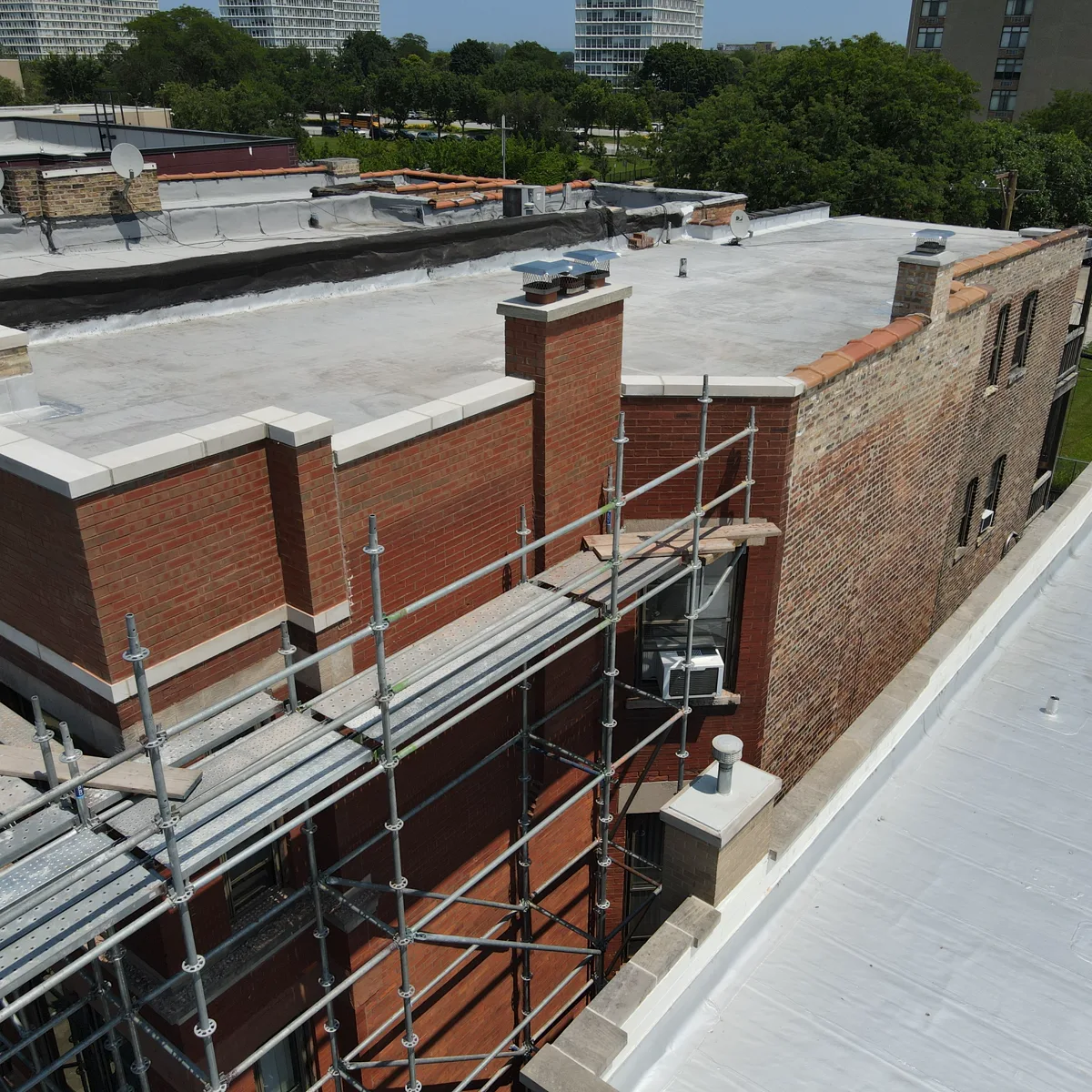 Scaffolded Chicago brick parapet wall mid-restoration with coping stones and roofline flashing exposed — Star Tuckpointing