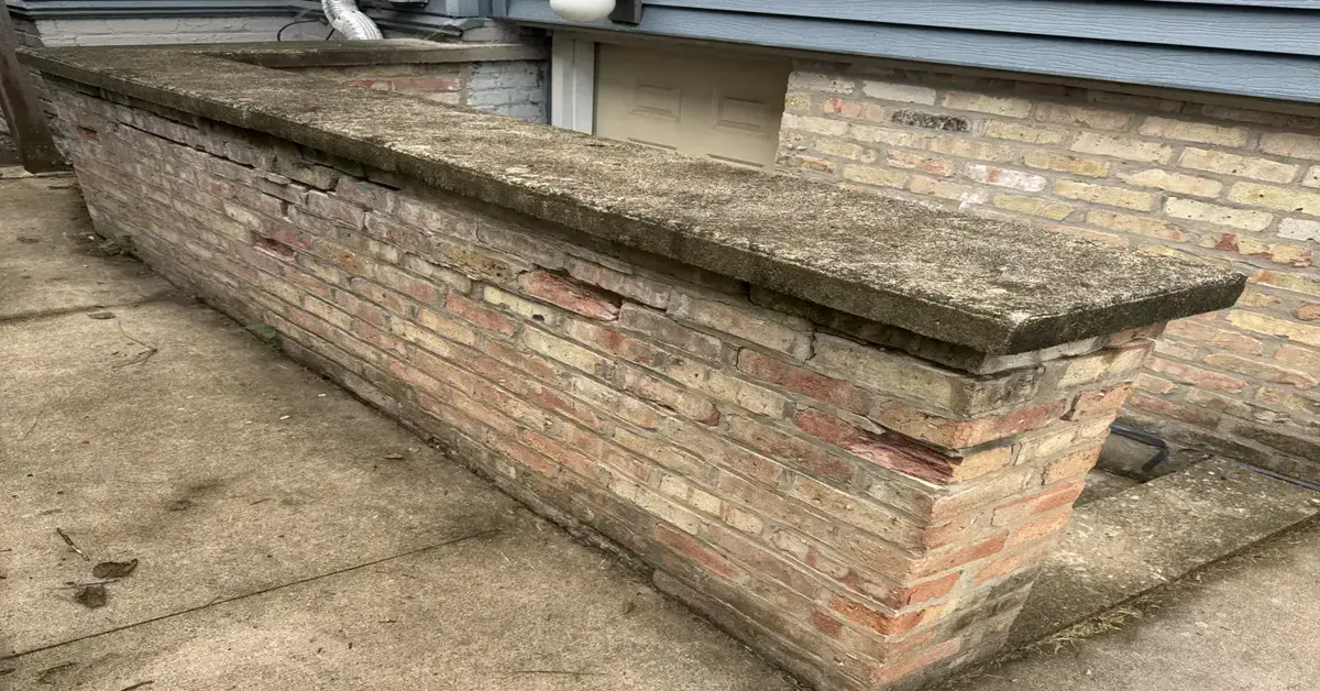 Corner column with damaged brick and failing mortar lines along the base of a Chicago building's stoop wall