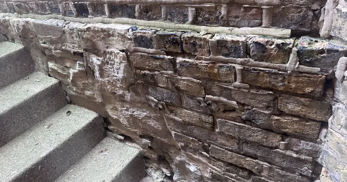 Failing mortar joints on a Chicago stoop wall: brick faces exposed where the surrounding mortar has washed out and joints have eroded away
