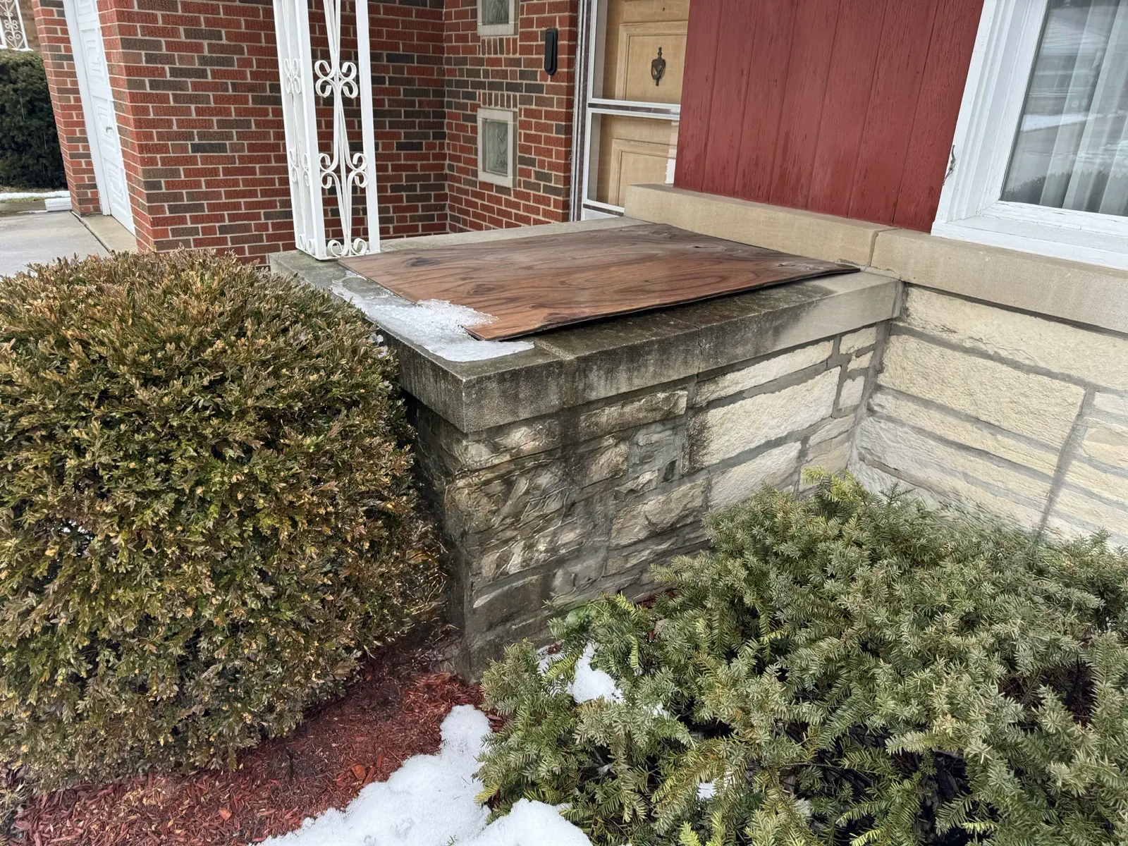 Damaged brick wingwall with weathered mortar joints and a boarded-up cap before masonry repair