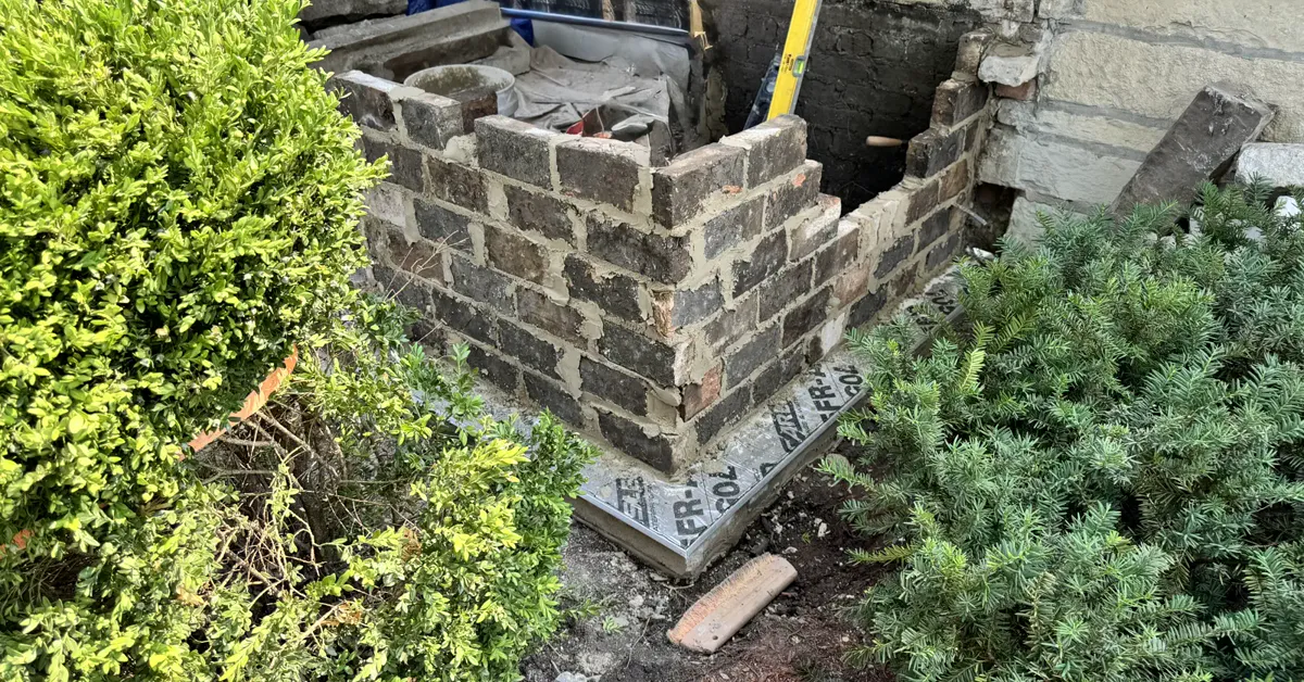 Wingwall mid-rebuild: courses of new brick being laid and reset against the existing foundation