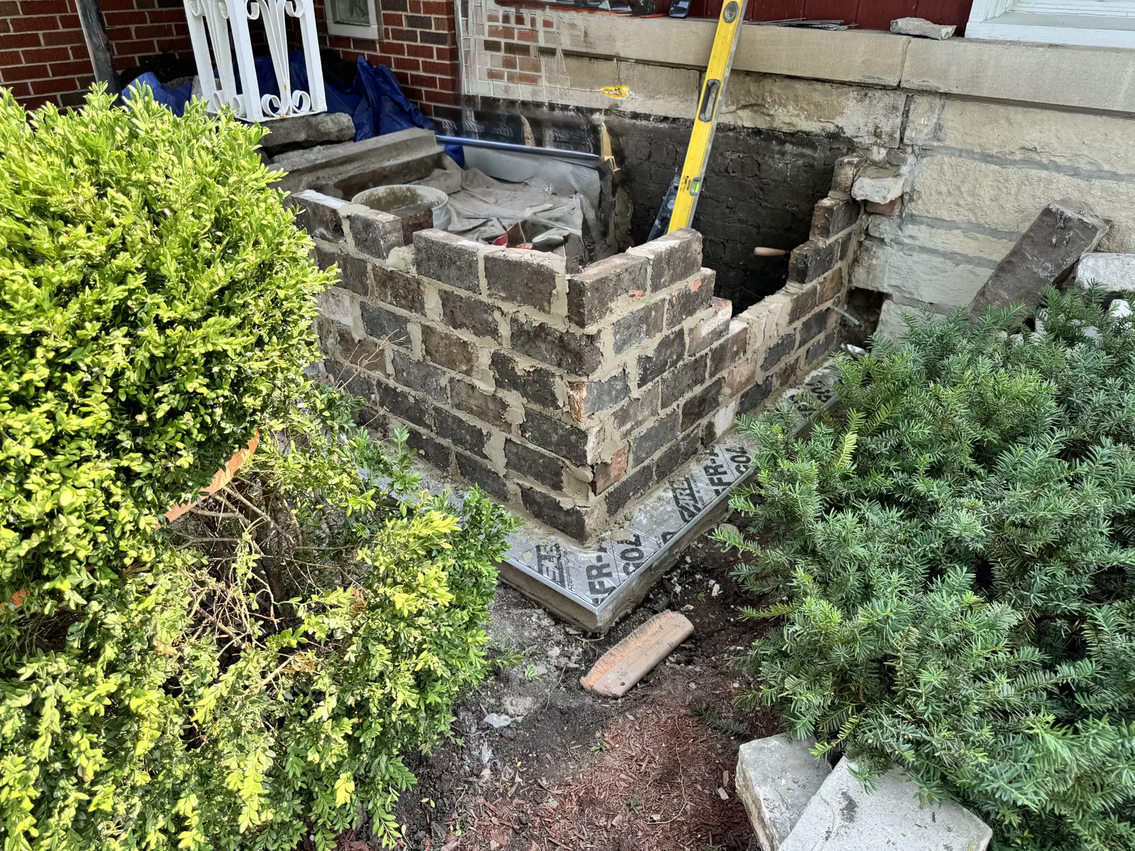 Wingwall mid-rebuild: courses of new brick being laid and reset against the existing foundation